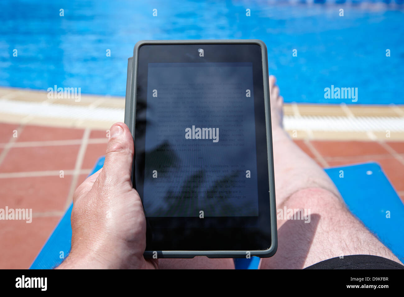 L'uomo la lettura di ebook su tablet PC dal lato di una piscina in vacanza Salou Costa Dorada Spagna Foto Stock