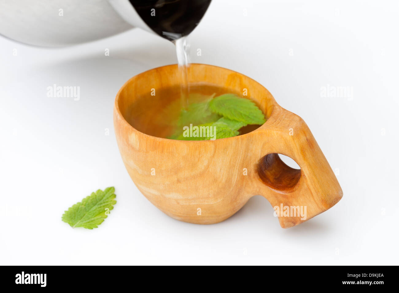 Acqua bollente che viene versato in una mano in legno intagliato contenenti Kuksa Melissa (Melissa officinalis) per fare il tè alle erbe Foto Stock