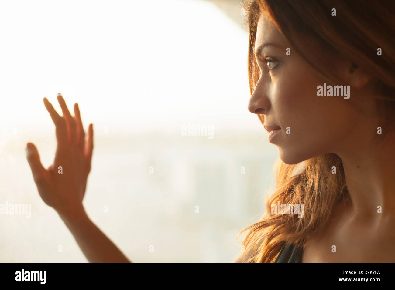 Giovane donna guardando fuori della finestra Foto Stock
