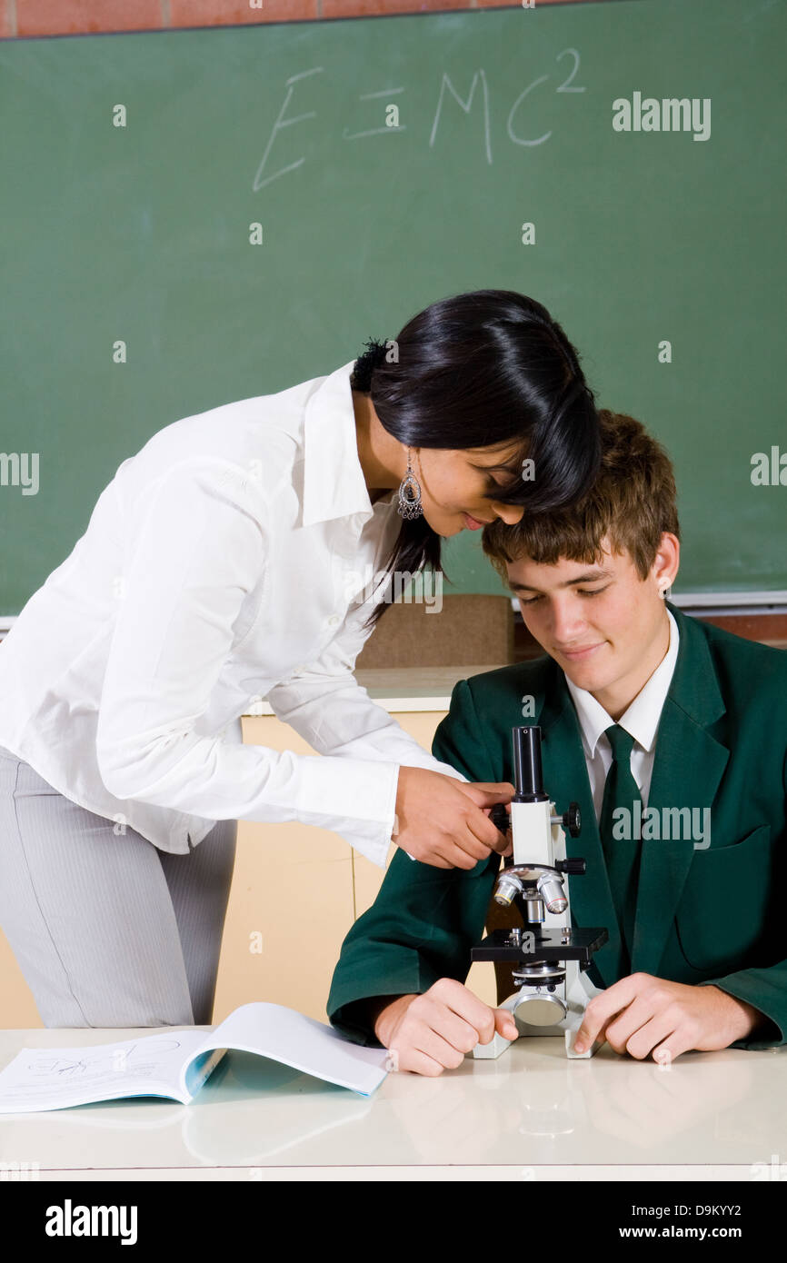 Giovane insegnante insegnamento studente di scuola superiore come utilizzare il microscopio Foto Stock