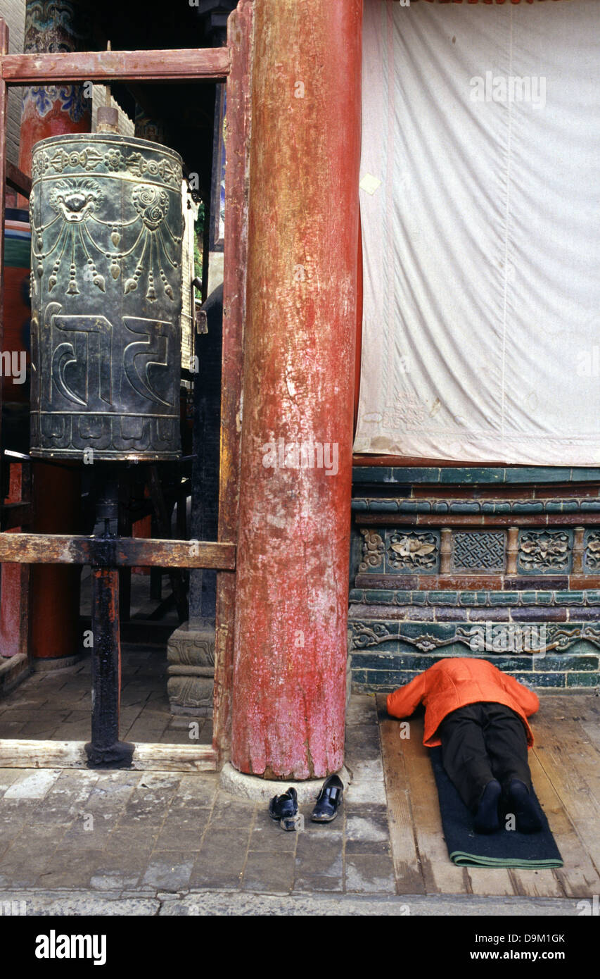 Buddista Tibetana adoratore prostrarsi accanto a Mani preghiera ruota in tibetano Kumbum gompa monastero chiamato anche Ta'er tempio fondata nel 1583 in una valle stretta vicino al villaggio di Lusar nella storica regione tibetana di Amdo nella contea di Huangzhong, in Xining la capitale della Provincia di Qinghai in Cina occidentale Foto Stock