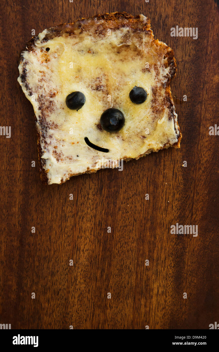 Tostare pezzo di pane con burro e miele, con la faccia fatta di mirtilli freschi. Foto Stock