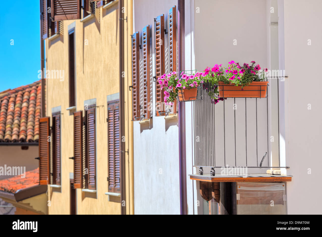 Fiori in vaso sul balcone di una tipica casa italiana con persiane di legno e un tetto di tegole nella città di La Morra in Italia. Foto Stock