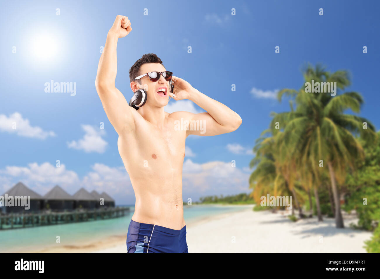 Happy guy ascoltando musica, su di una spiaggia di sabbia con palme e acqua villa cottages a Kuredu island, Maldive Foto Stock