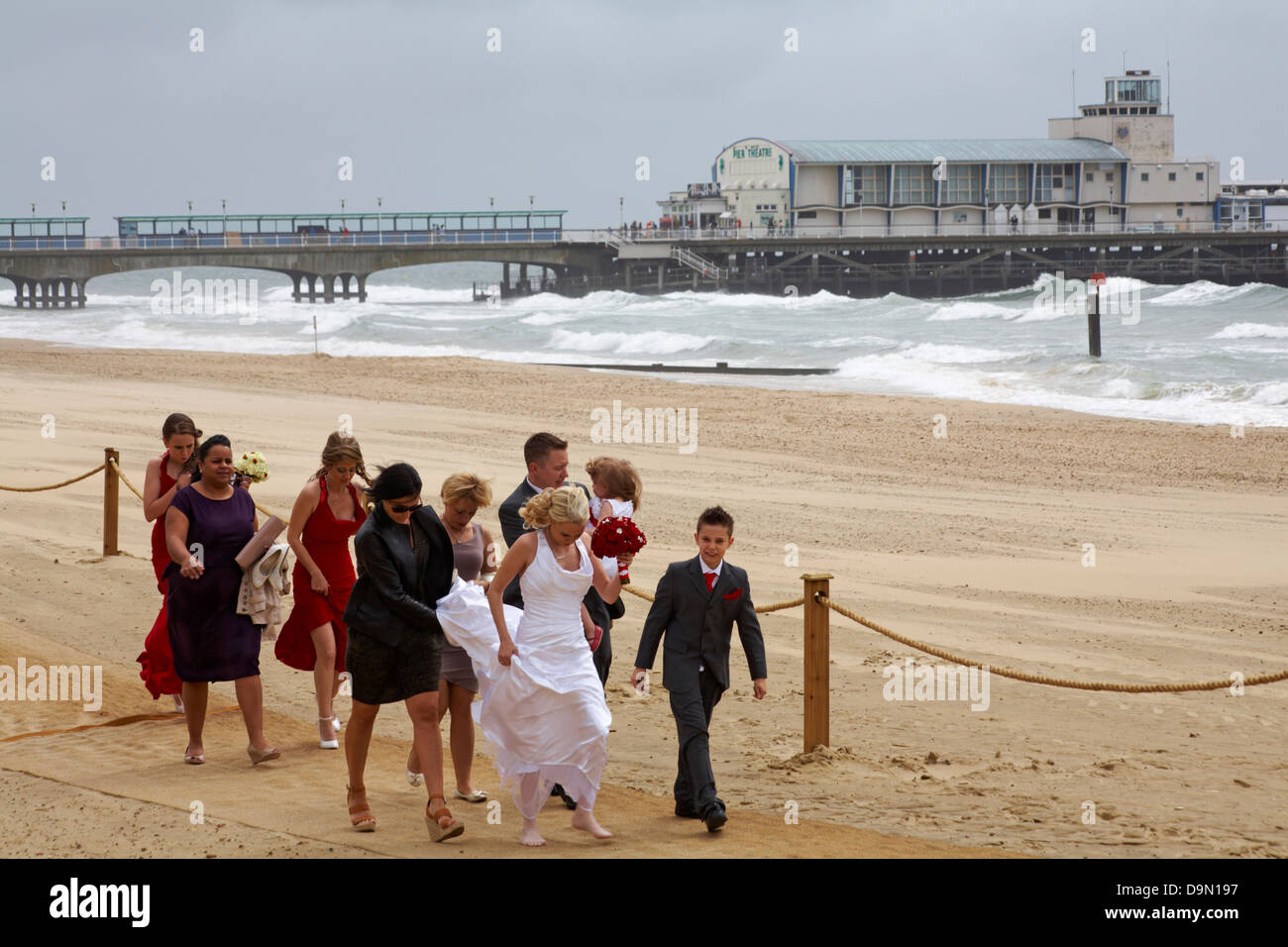 Festa nuziale, sposa e damigella arrivando alla cerimonia di nozze su Bournemouth Beach in una giornata di vento in giugno Foto Stock