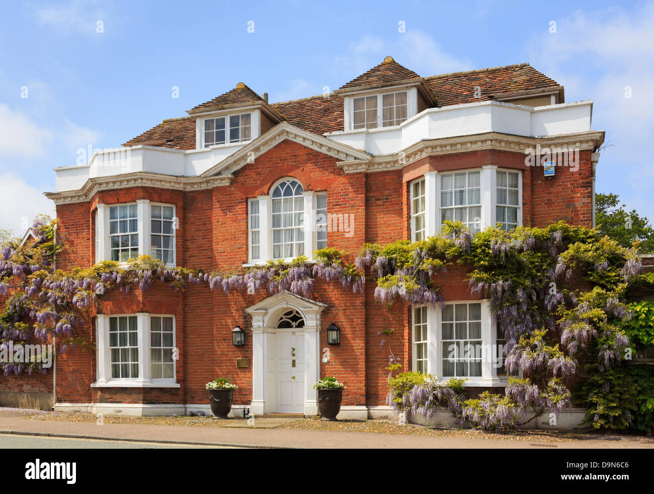 Il Glicine floribunda crescente attorno ad un rosso-mattone Georgian casa indipendente anteriore nel pittoresco villaggio in estate. Lavenham Suffolk England Regno Unito Gran Bretagna Foto Stock