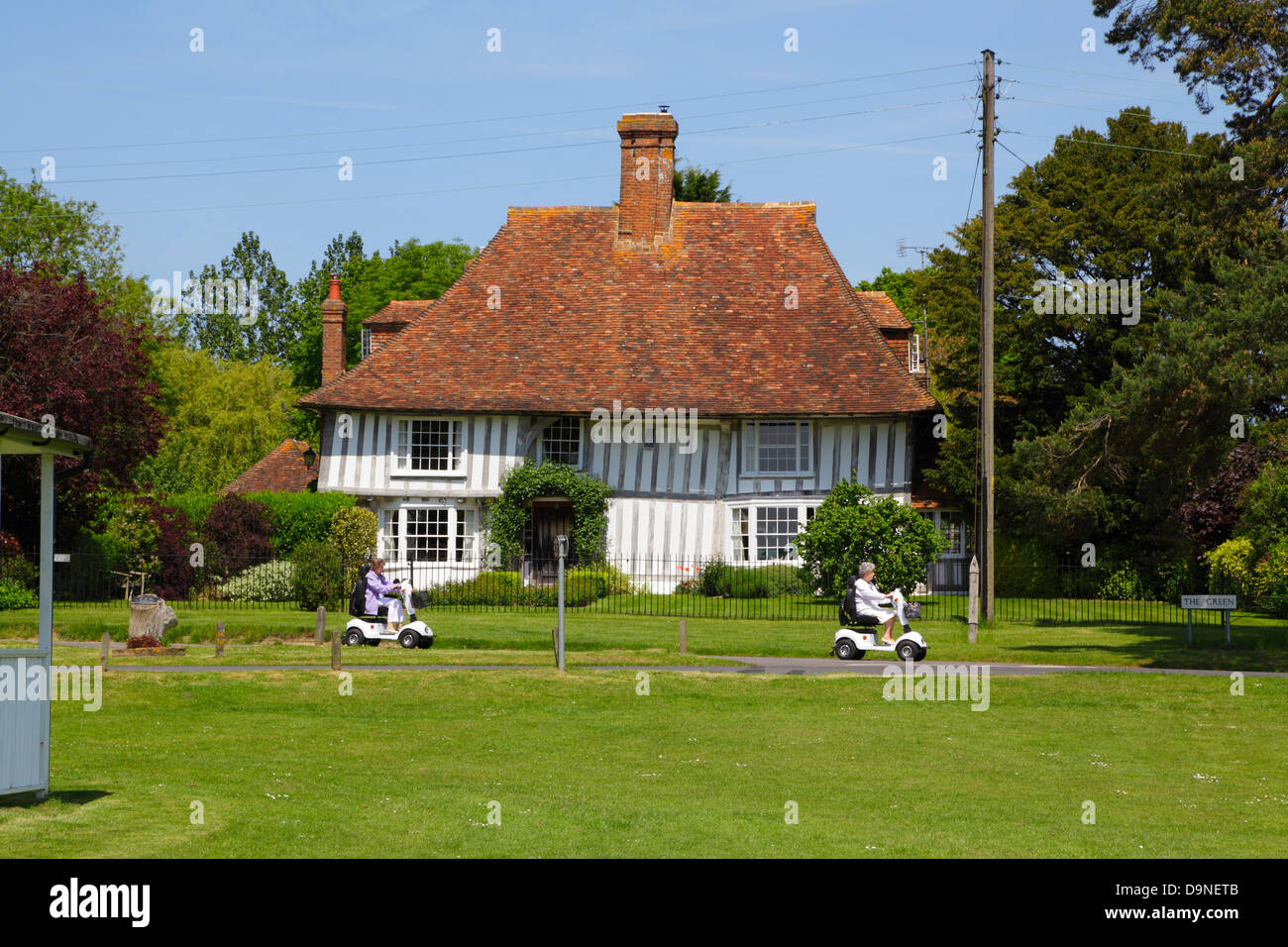 Due signore sulla mobilità di scooter a cavallo lungo il verde, Woodchurch Kent England Regno Unito GB Foto Stock