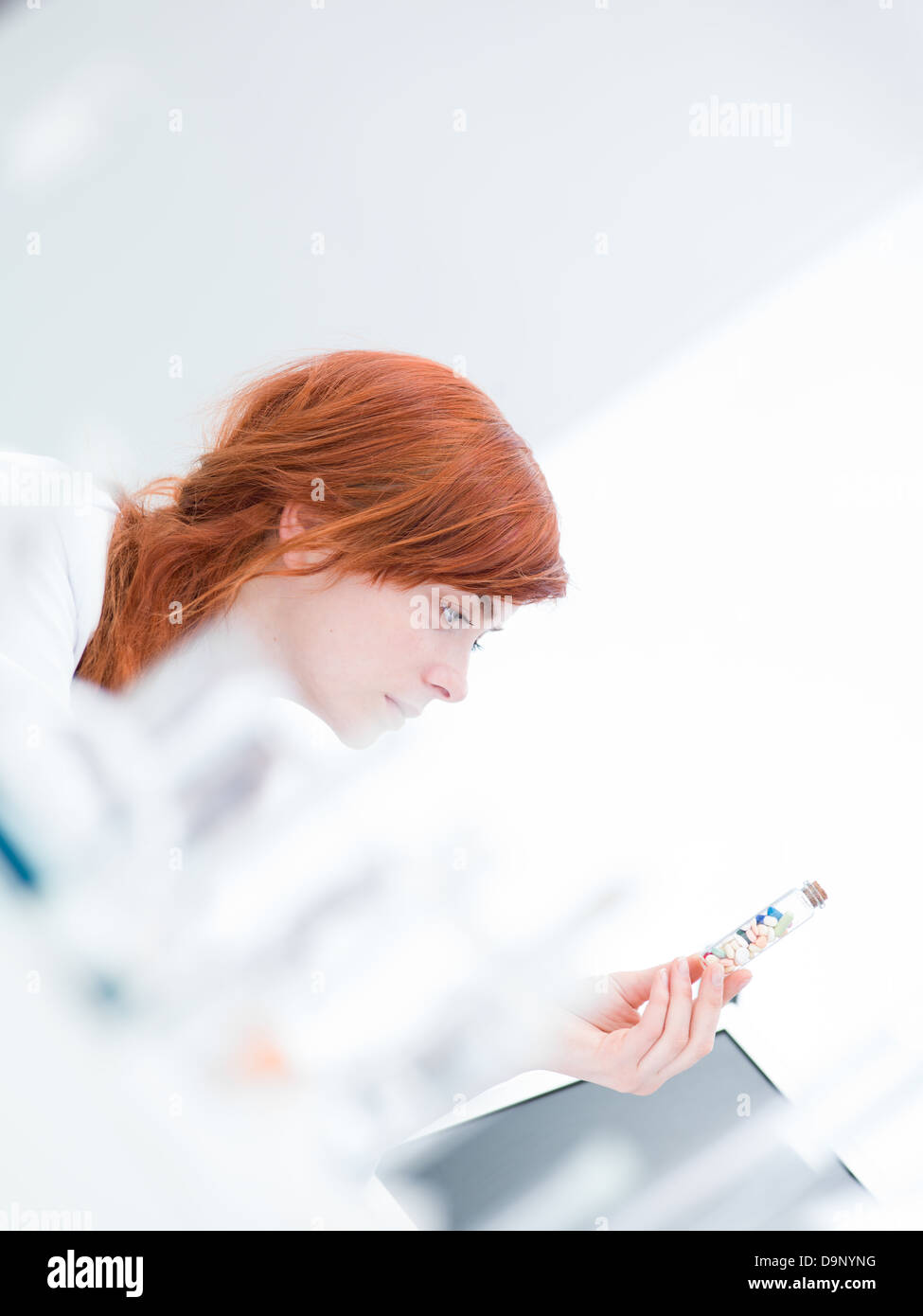 Laboratorio sfocata vista laterale di una donna analizzando le pillole in un tubo Foto Stock