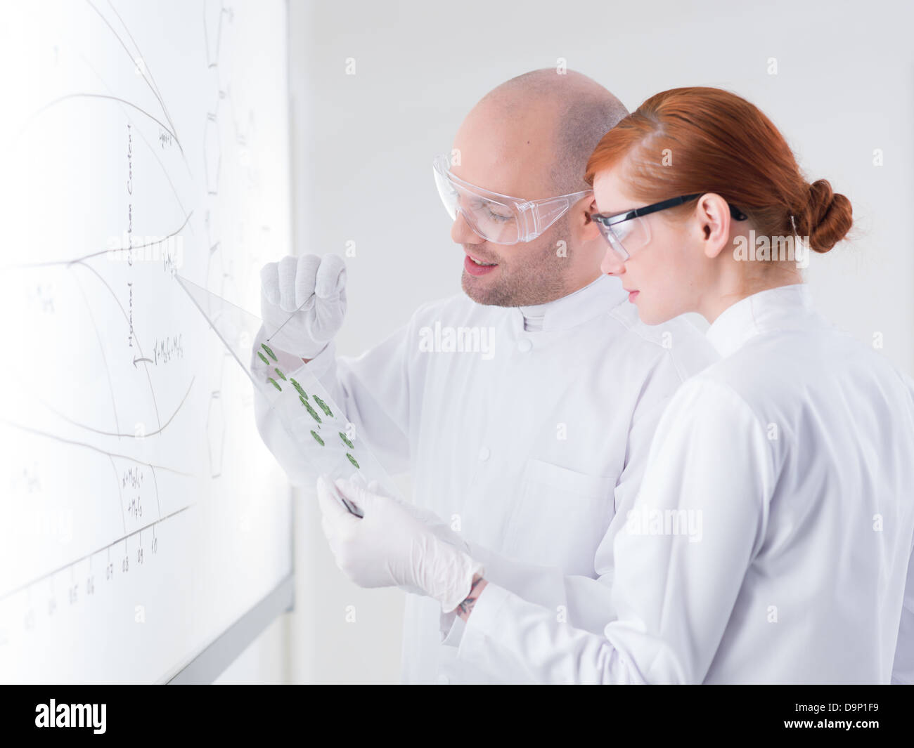 Close-up di un insegnante in un laboratorio di chimica che mostra alcuni campioni al suo allievo di fronte a una lavagna Foto Stock