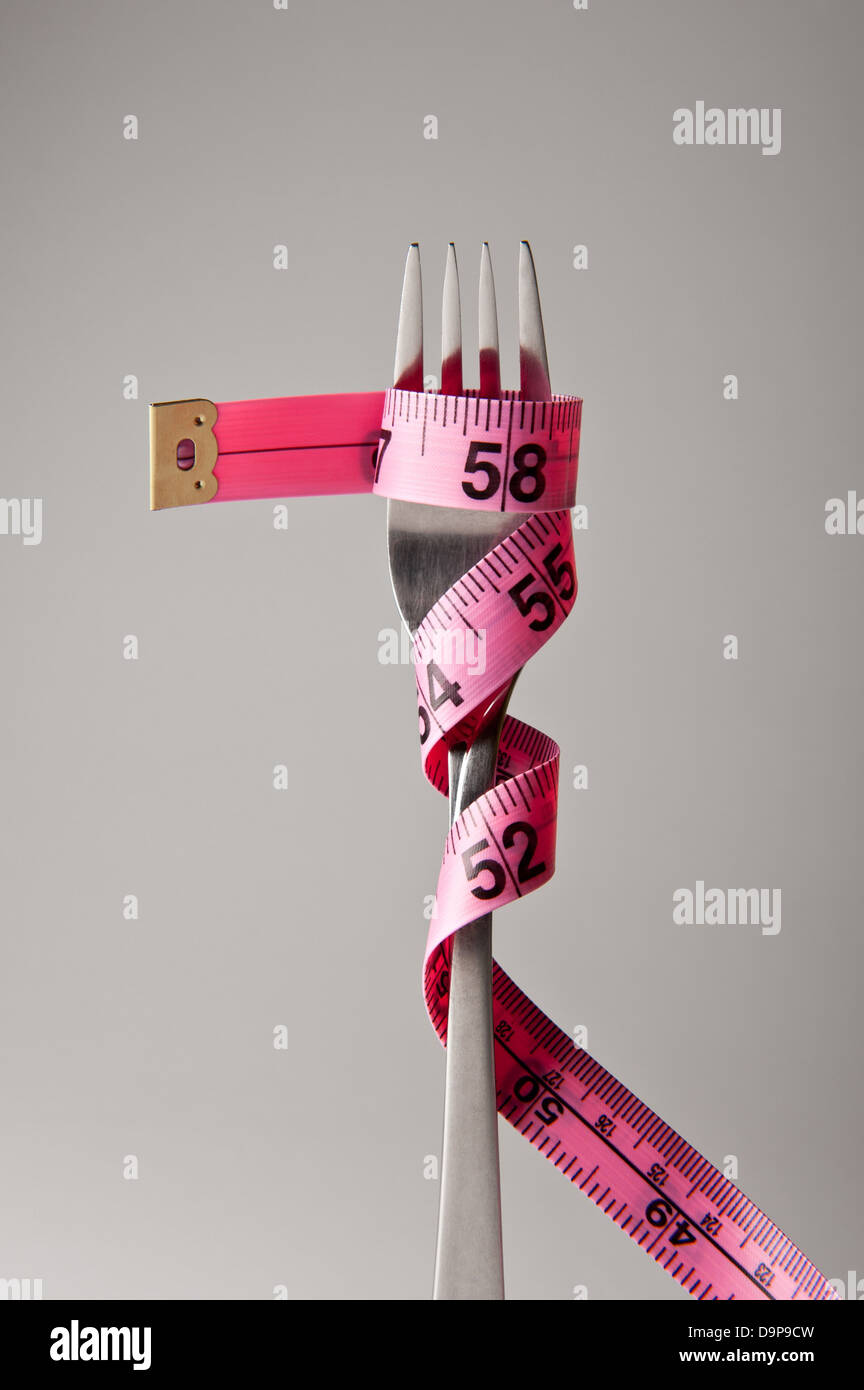 Una singola forcella in argento con rosa misurando il nastro avvolto intorno ad esso relative ad una rigida dieta o mangiare sano piano. Foto Stock