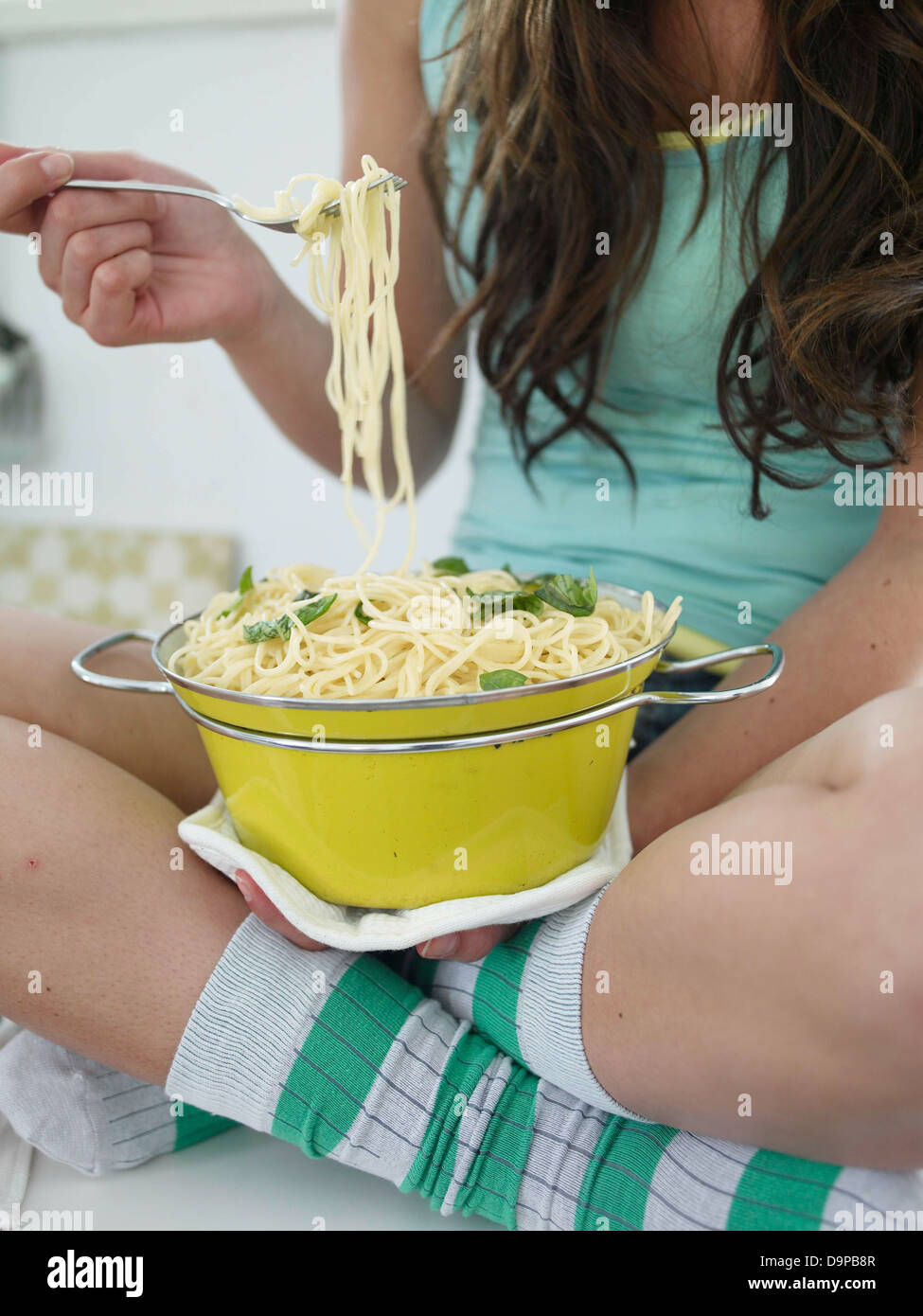 Giovane donna seduta sul banco di cucina mangiare spaghetti Foto Stock