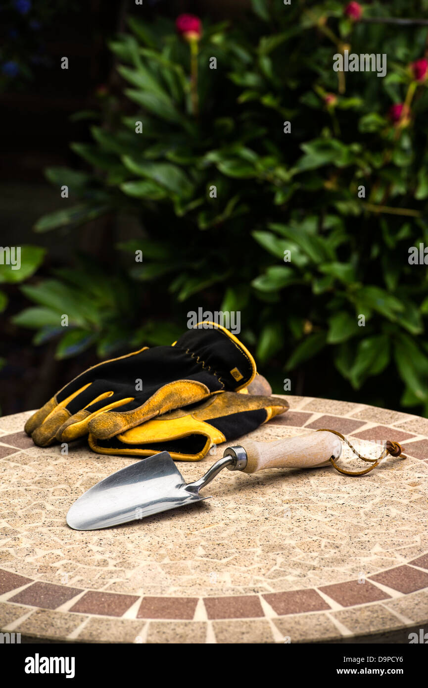 Cazzuola a mano con i guanti su un tavolo da giardino. Foto Stock