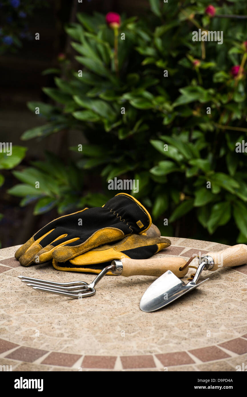 Forcella a mano e cazzuola, con guanti su un tavolo da giardino. Foto Stock