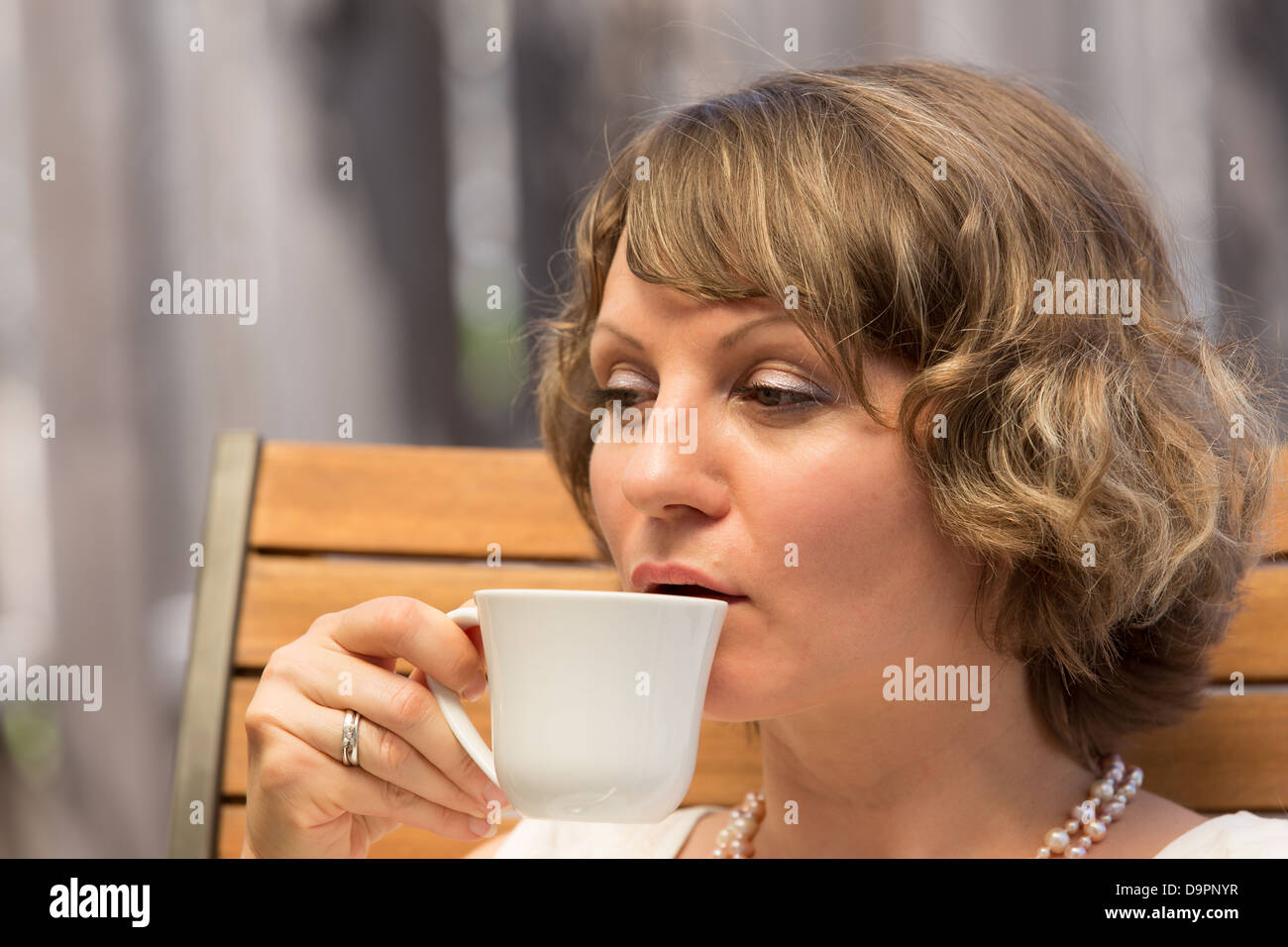 Donna attraente di bere una tazza di caffè sulla sedia in legno. Foto Stock