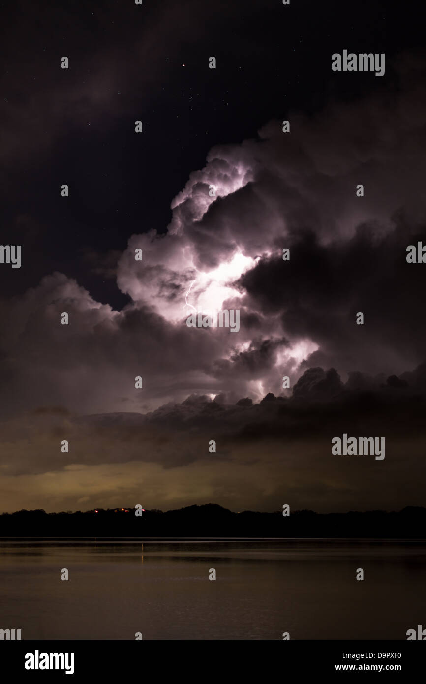 Tempesta riflettendo sulle sponde di un lago. Il fulmine lampeggia con un cielo stellato sopra Foto Stock