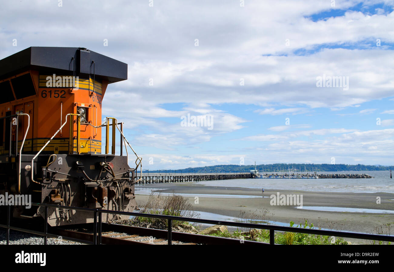 Locomotiva del treno in movimento lungo la ferrovia BNSF linea che segue la spiaggia di roccia bianca, BC, Canada. Anche pier nella baia di confine. Foto Stock