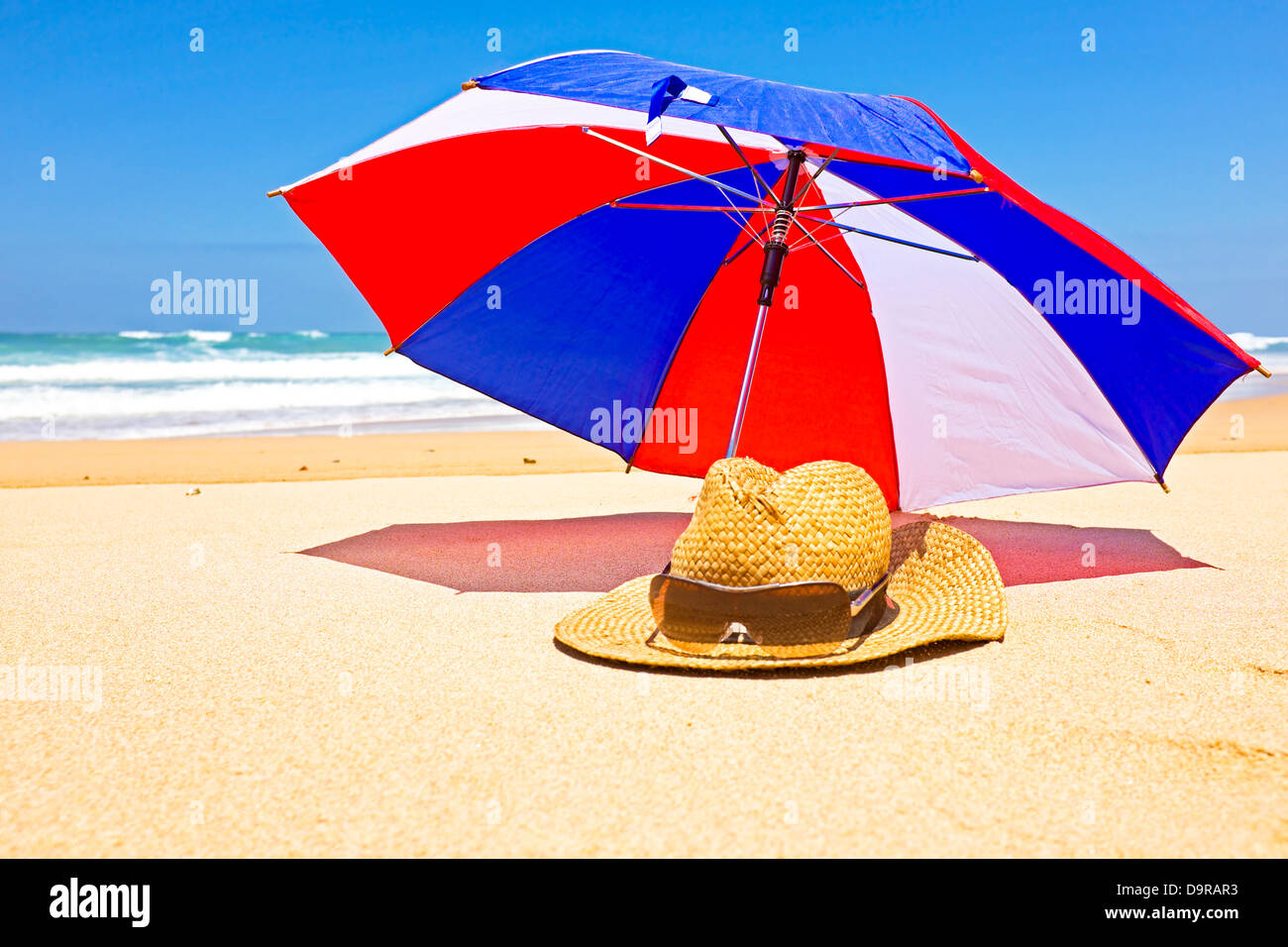 Cappello di paglia, occhiali da sole e ombrellone in spiaggia Foto Stock