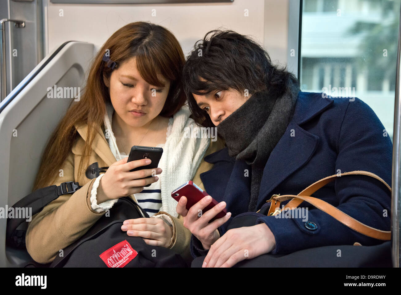 Coppia giovane con telefoni cellulari sulla metropolitana di Tokyo Foto Stock