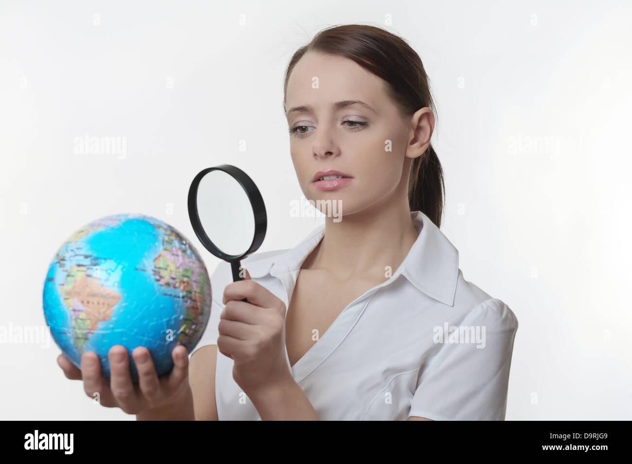 Donna che mantiene un globo di Jigsaw Puzzle e lo sta guardando con un occhio di ispezione con una lente di ingrandimento Foto Stock