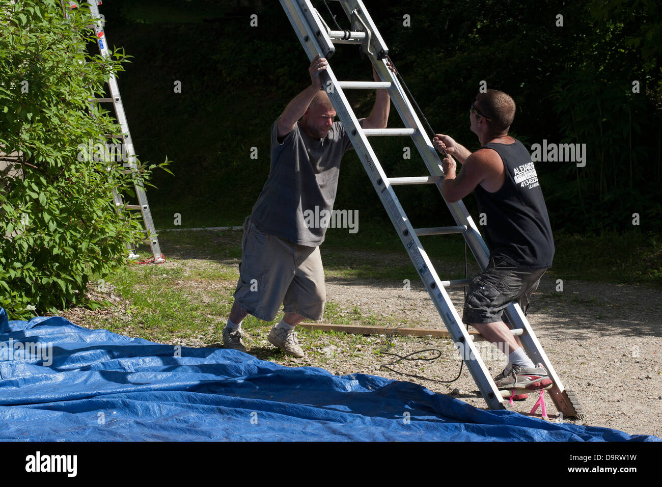 Su un pomeriggio d'estate, due uomini pulizia dopo un lavoro di verniciatura. Essi si stanno muovendo la loro estensione scaletta prima di lasciare il posto di lavoro. Foto Stock