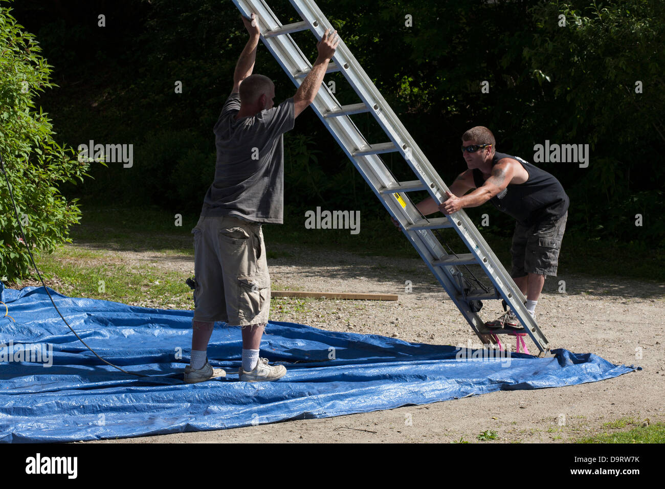 Su un pomeriggio d'estate, due uomini pulizia dopo un lavoro di verniciatura. Essi si stanno muovendo la loro estensione scaletta prima di lasciare il posto di lavoro. Foto Stock