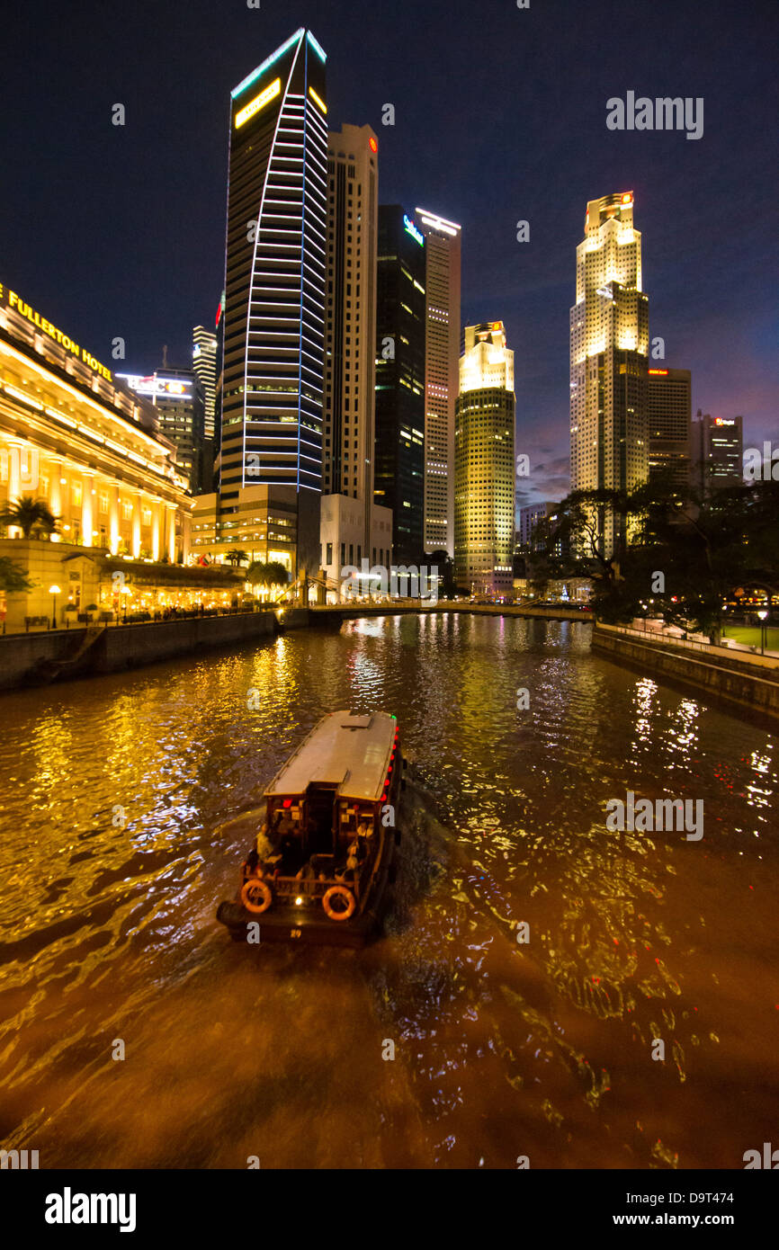 Il Cavenagh Bridge, una barca sul fiume Singapore, il Fullerton Hotel e il quartiere centrale degli affari di notte, Singapore Foto Stock