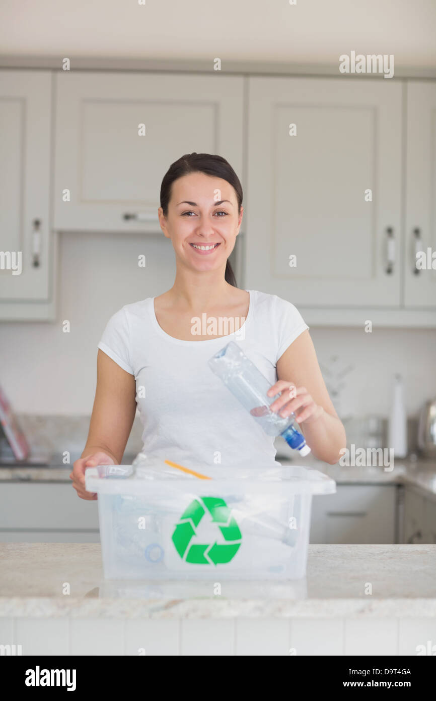 Donna sorridente di gettare la bottiglia nel contenitore di riciclaggio Foto Stock