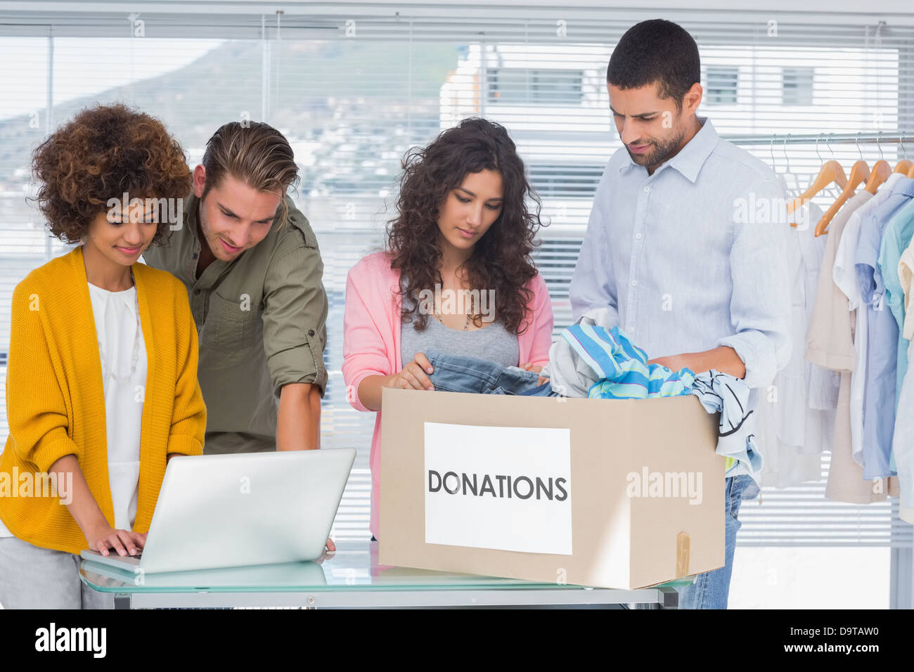 Volontari utilizzando un computer portatile e di prendere i vestiti da charity box Foto Stock