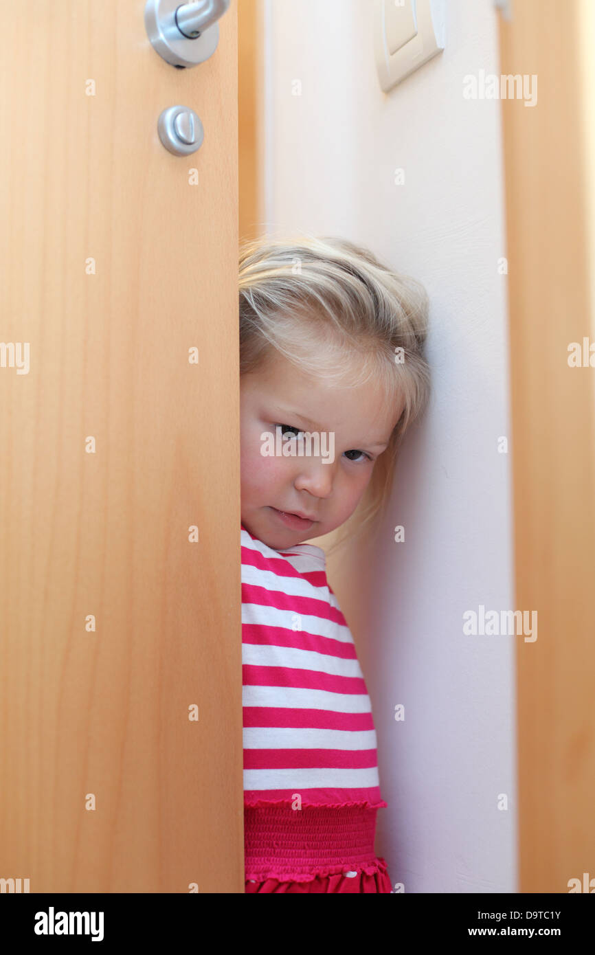 Timida ragazzina di nascondersi dietro la porta Foto Stock