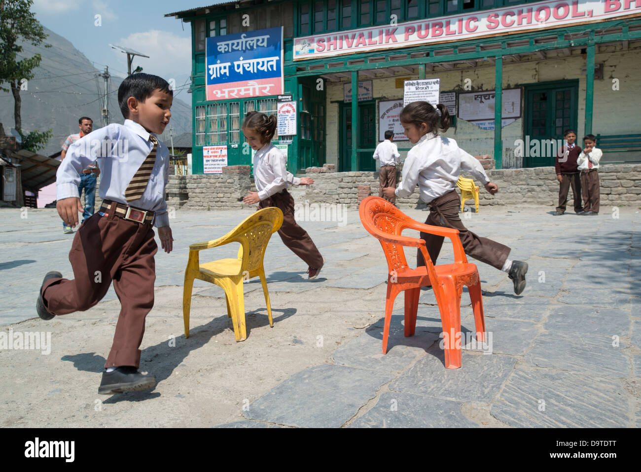 Indian bambini delle scuole elementari un gioco delle sedie musicali nella piazza del villaggio a Bharmour, Himachal Pradesh, India Foto Stock