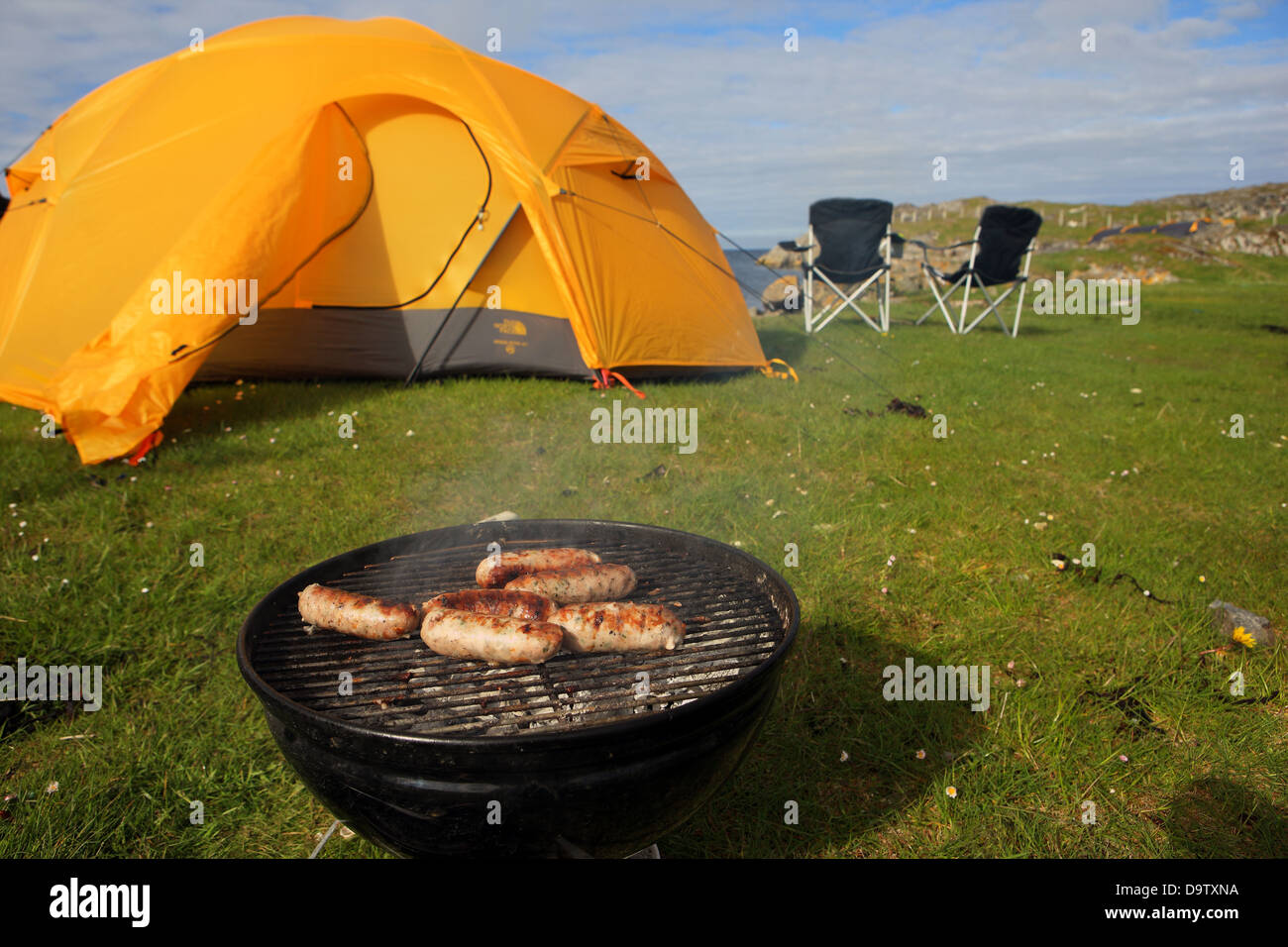Salsicce durate la cottura campeggio con tenda e sedie da mare in Scozia Foto Stock