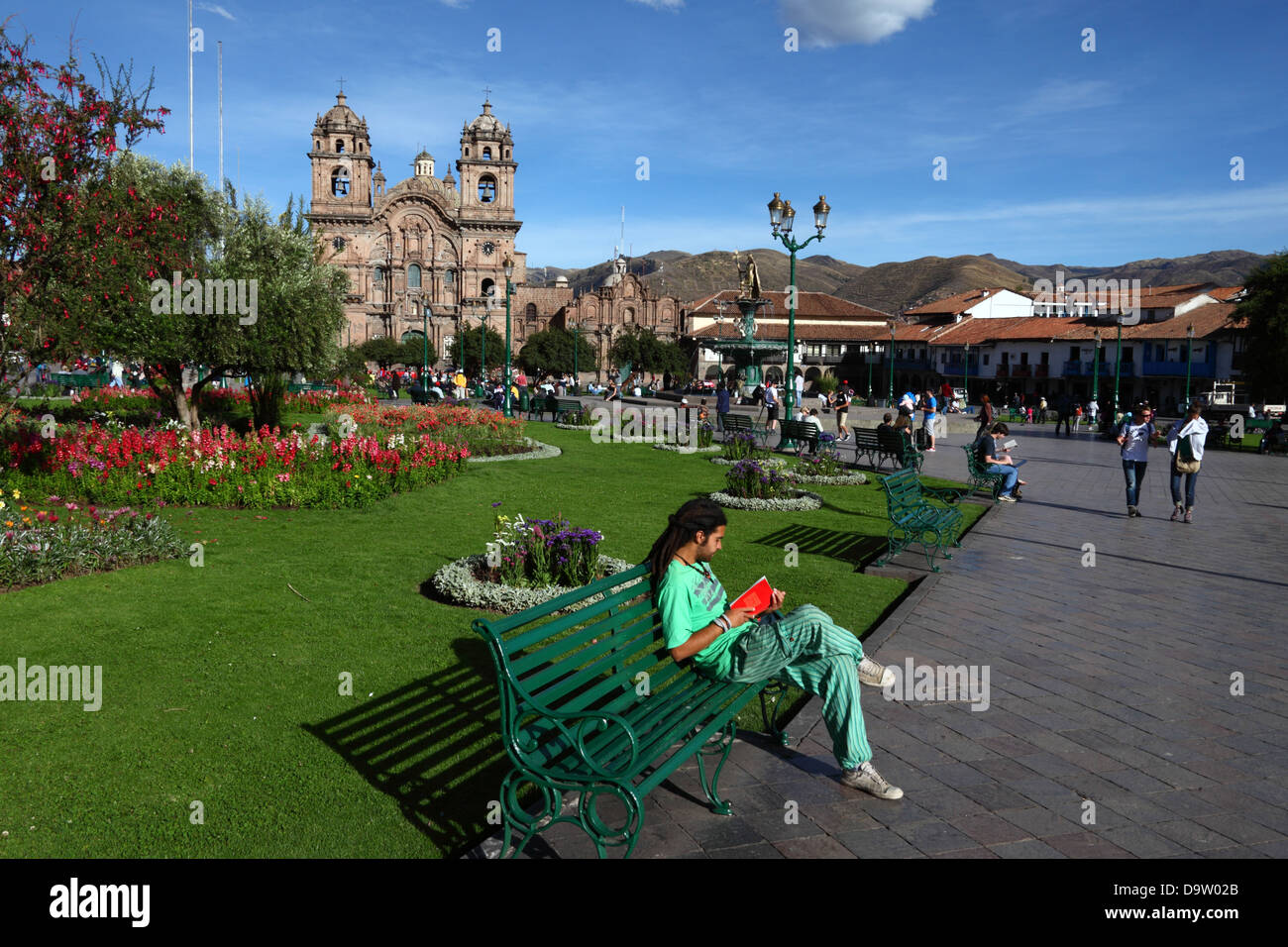 Backpacker seduto sulla panchina a leggere un libro, la chiesa di Compañia de Jesus sullo sfondo, Plaza de Armas, Cusco, Perù Foto Stock