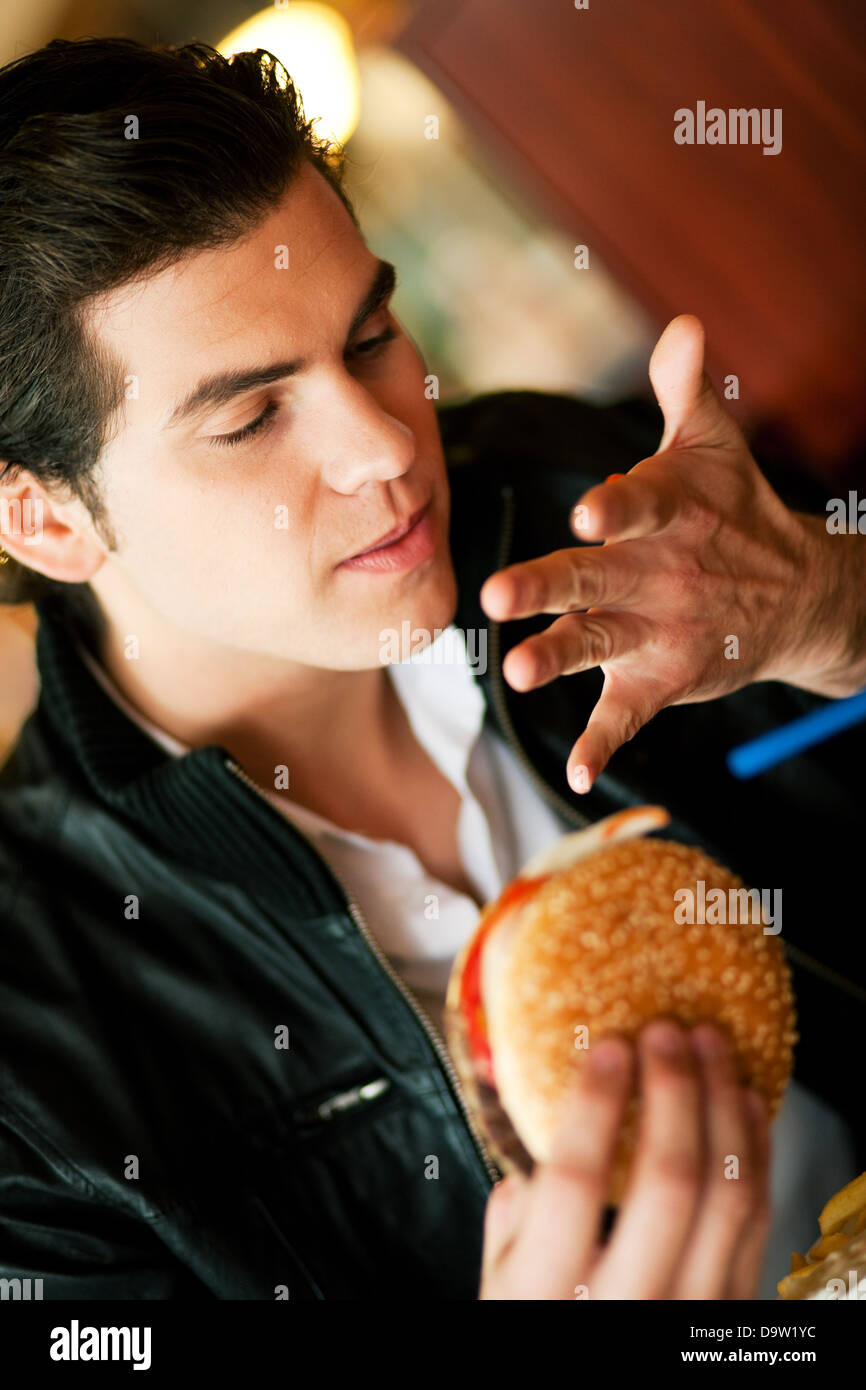 Uomo in un ristorante o una cena di mangiare un hamburger, è così bene che egli fa leccare le sue dita, girato con la luce disponibile Foto Stock