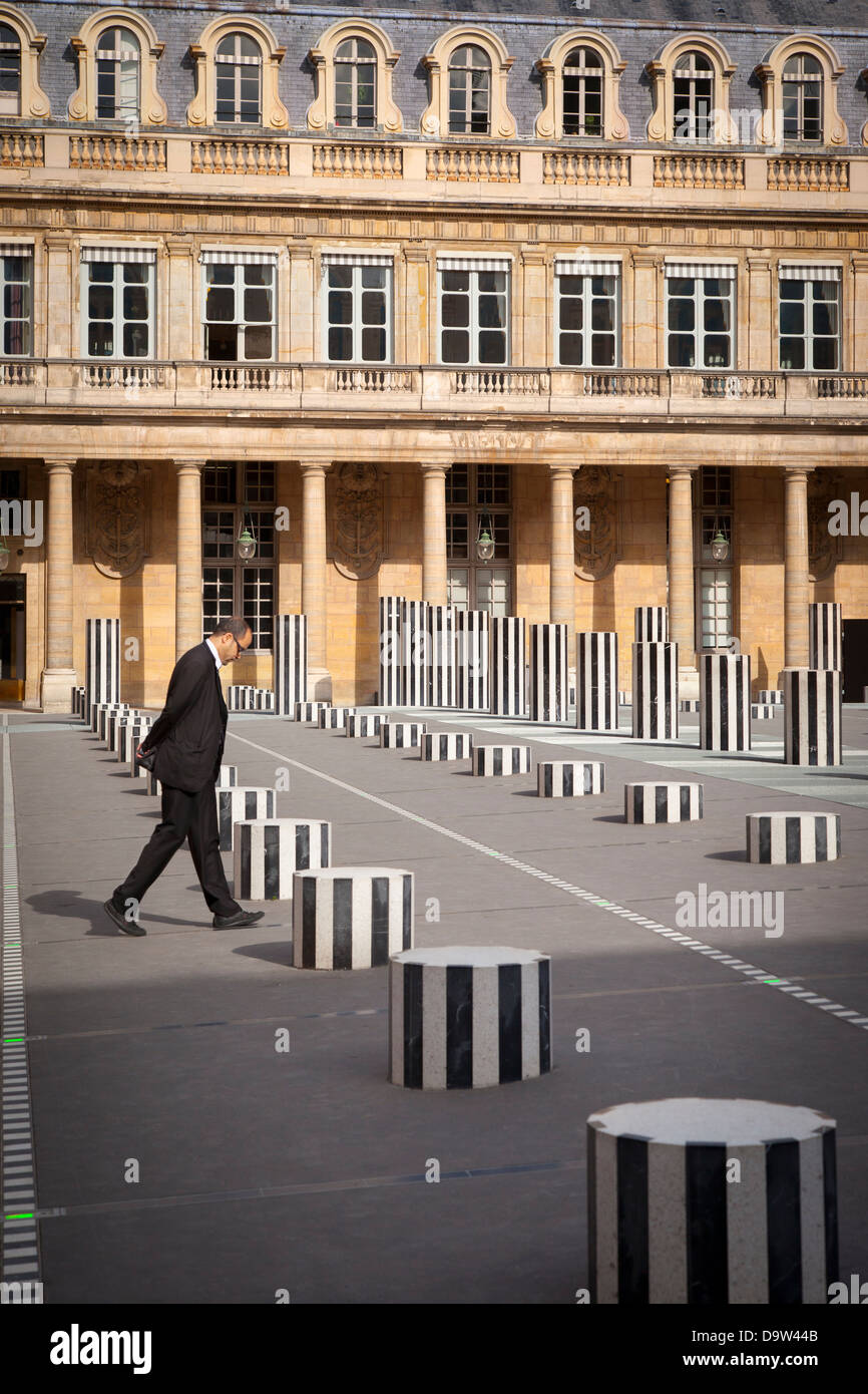 Uomo in business suit passeggiate attraverso il cortile del Palais Royal, con Daniel Buren creato colonne, Parigi Francia Foto Stock