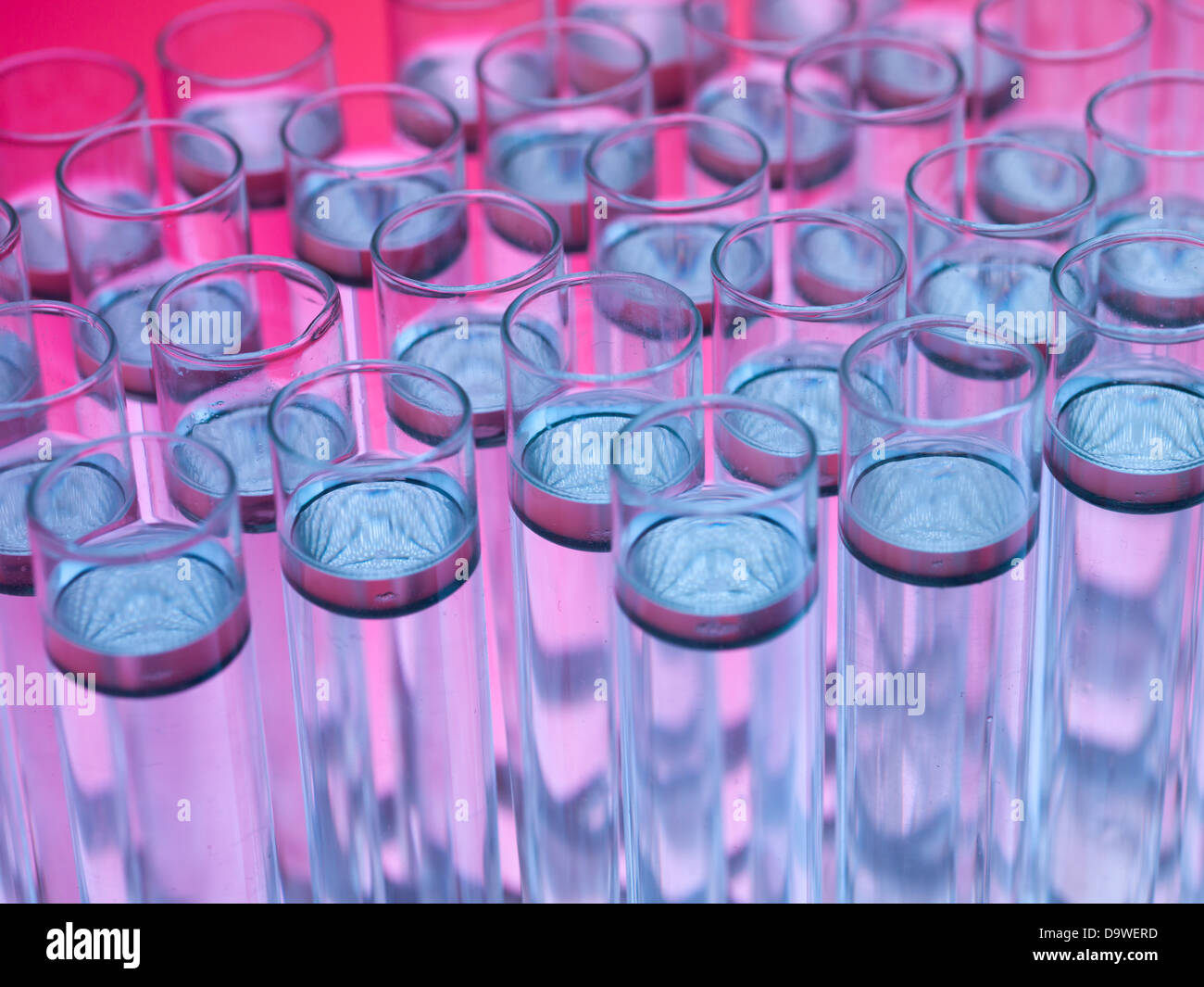 Vista aerea, macro di provette riempite con trasparente scuro sostanza galleggiante nel liquido incolore, contro un gradiente di colore rosa e sfondo viola Foto Stock