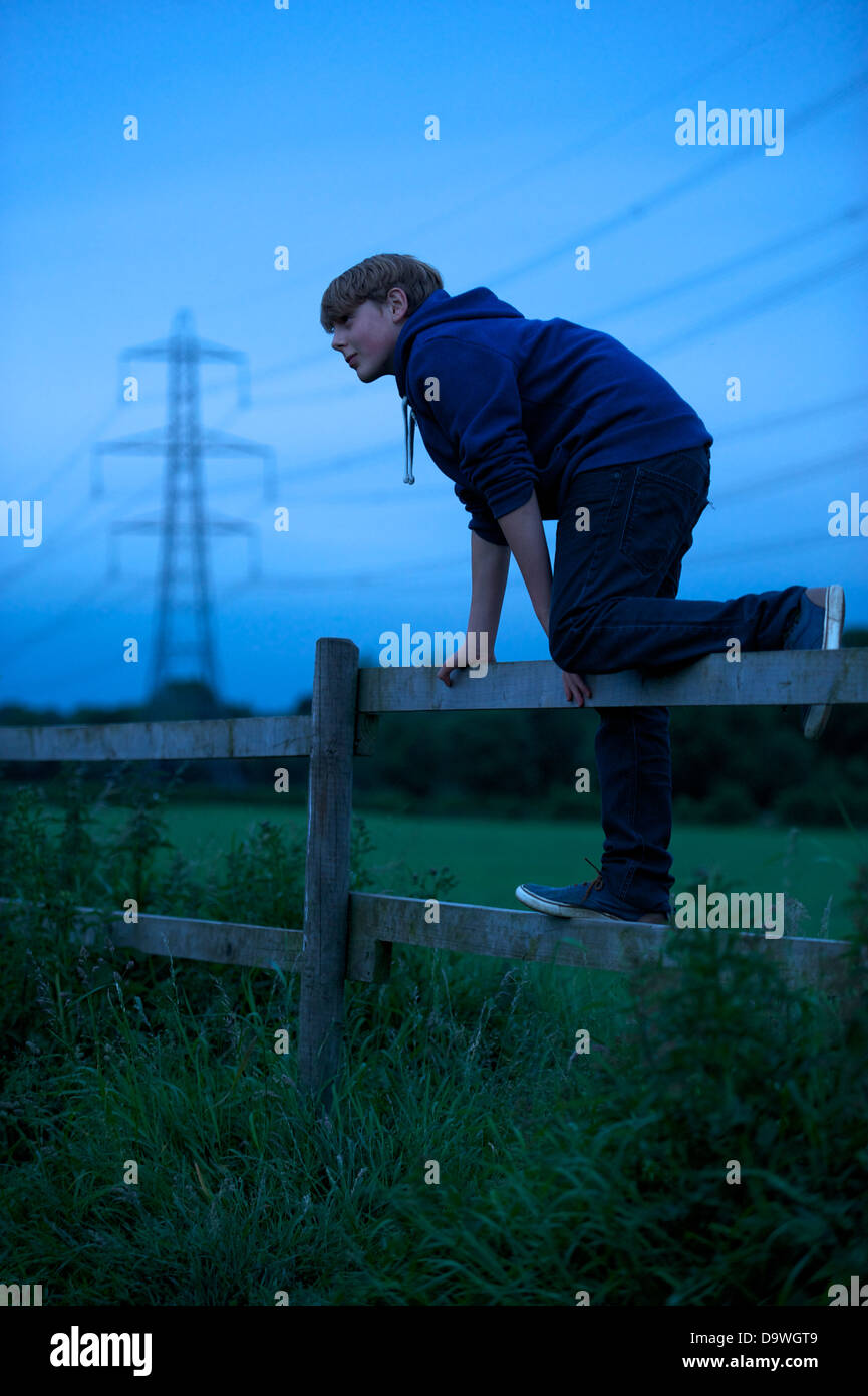 Un giovane ragazzo si arrampica su un recinto con linee elettriche in background Foto Stock