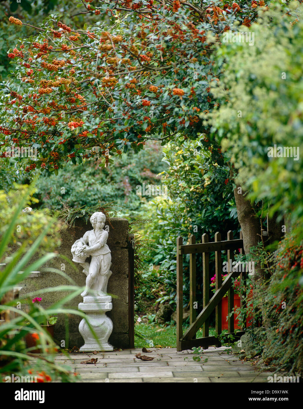 Statua del giardino accanto al cancello aperto sovrastata con alberi Foto Stock