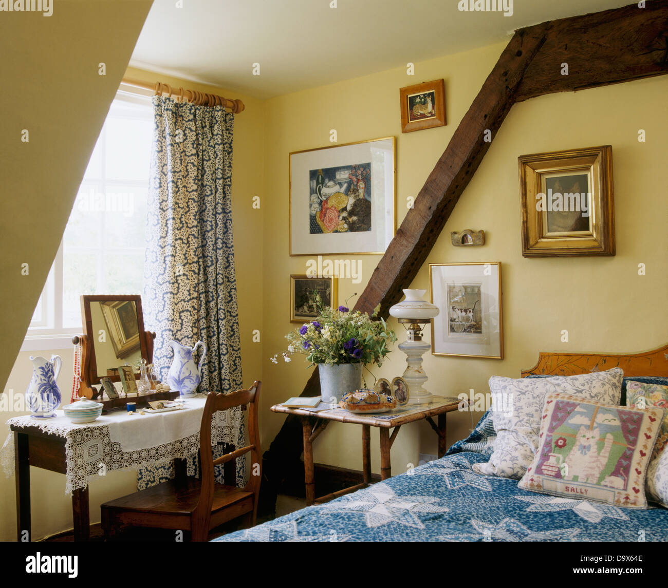 Il cane dorme sul letto con cuscini e coperchio blu in cottage camera da letto con pareti in legno fascio e toeletta nella parte anteriore della finestra Foto Stock