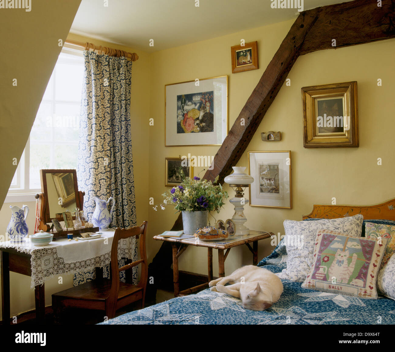 Il cane dorme sul letto con cuscini e coperchio blu in cottage camera da letto con pareti in legno fascio e toeletta nella parte anteriore della finestra Foto Stock