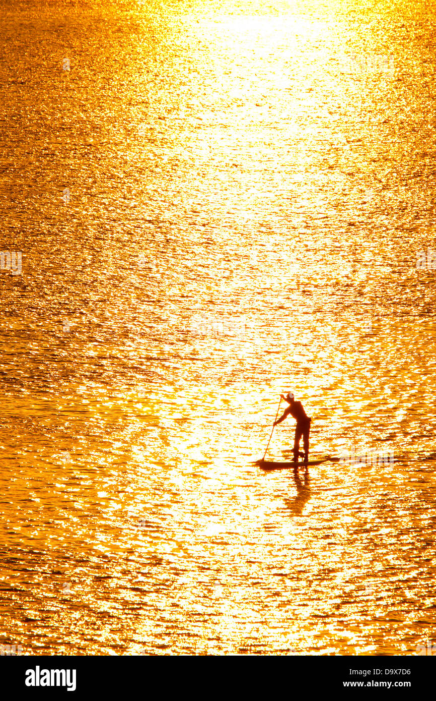 L'uomo paddleboarding in acque aperte al tramonto Foto Stock