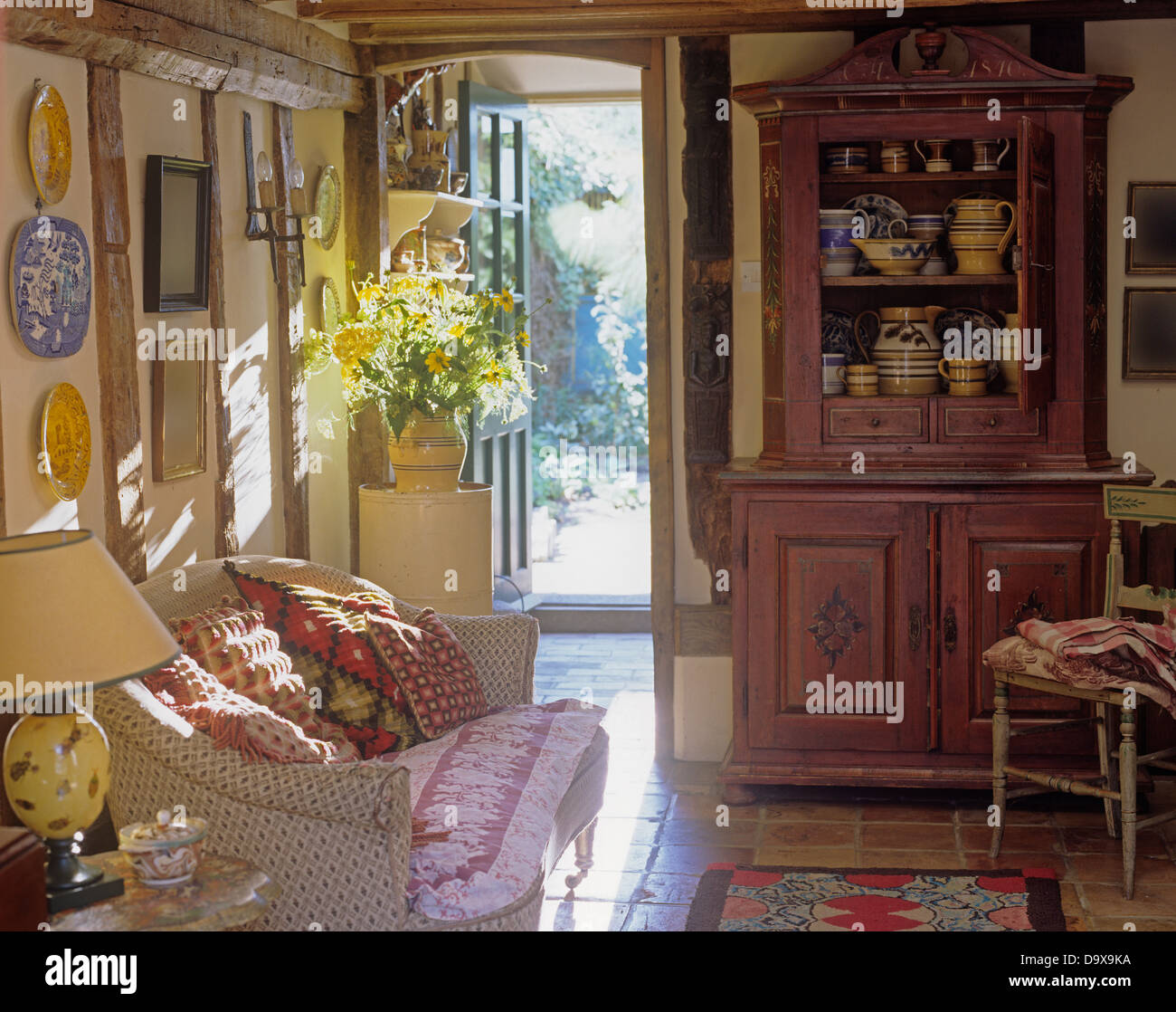 Pino verniciato comò e divani floreali impilati con cuscini in cottage in salotto con porta anteriore aperta Foto Stock