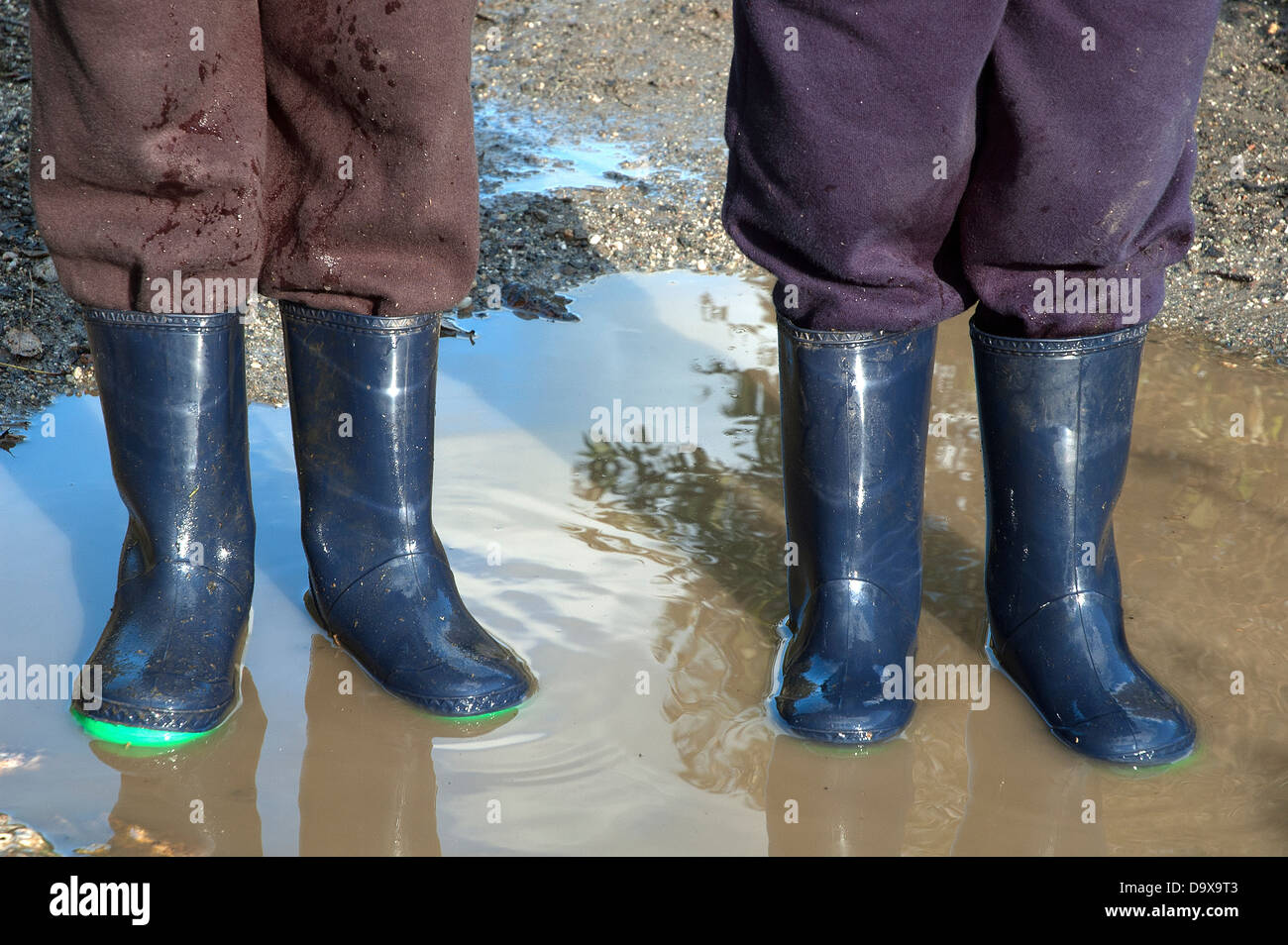 Due bambini in piedi in una pozza di acqua piovana di indossare gli stivali da pioggia Foto Stock