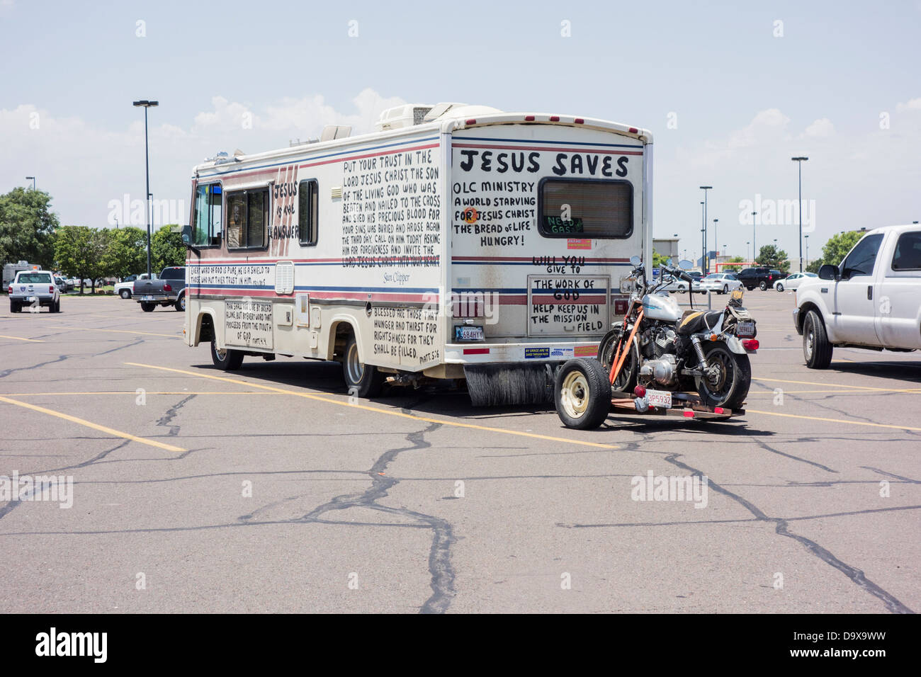 Un vecchio veicolo per attività ricreative di traino di un motociclo e dipinte a mano e con scrittura biblica si siede in un parcheggio. Foto Stock