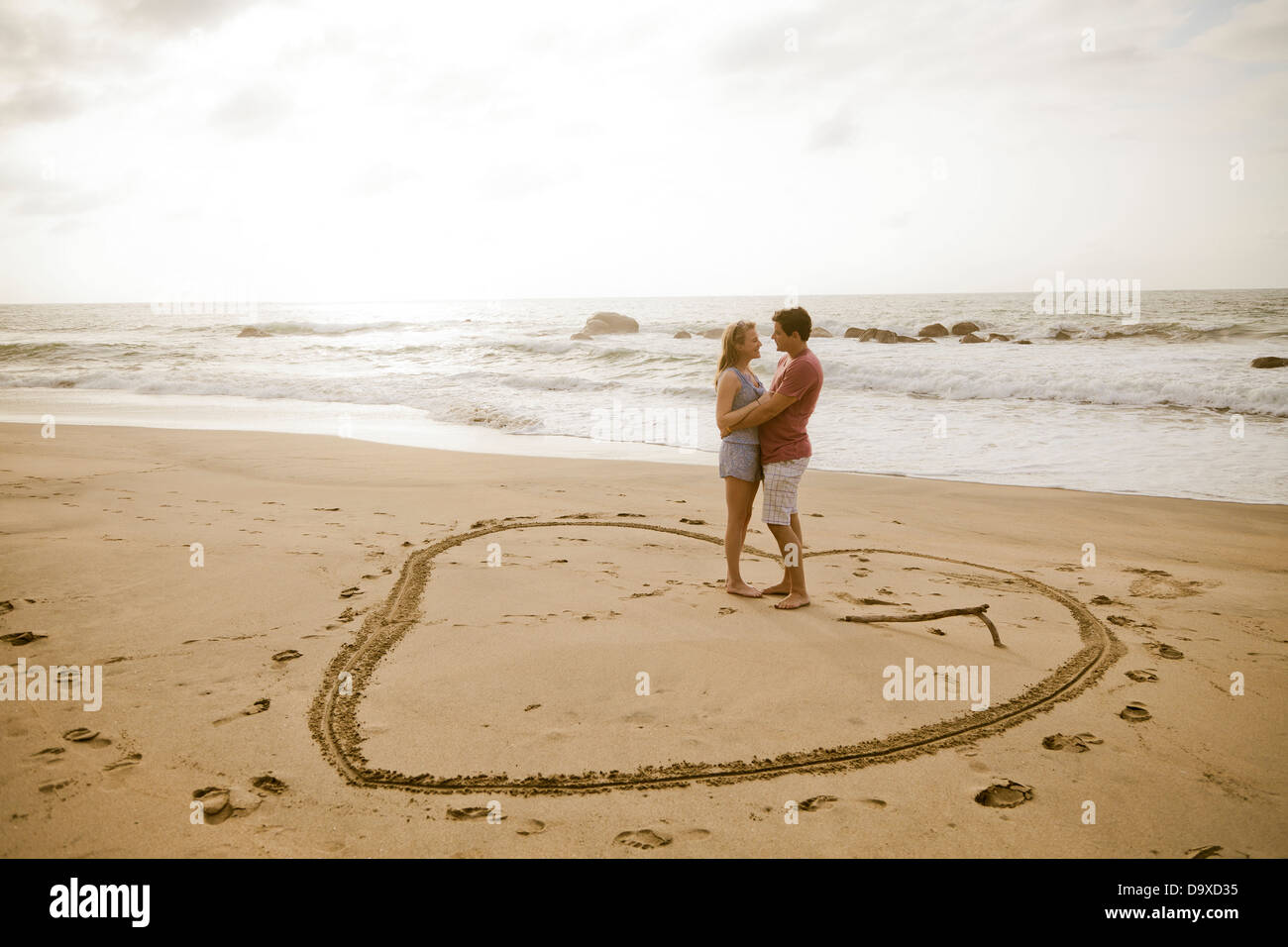 Coppia giovane in piedi nel cuore disegno sulla spiaggia Foto Stock