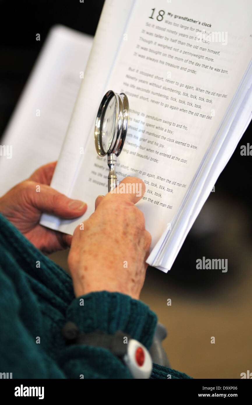 Una donna con demenza utilizza una lente di ingrandimento per vedere la musica in una classe di canto per persone anziane con demenza. Foto Stock