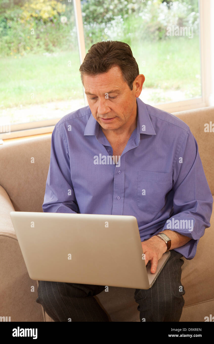 Buona ricerca uomo di mezza età seduto su un divano con un notebook. Foto Stock