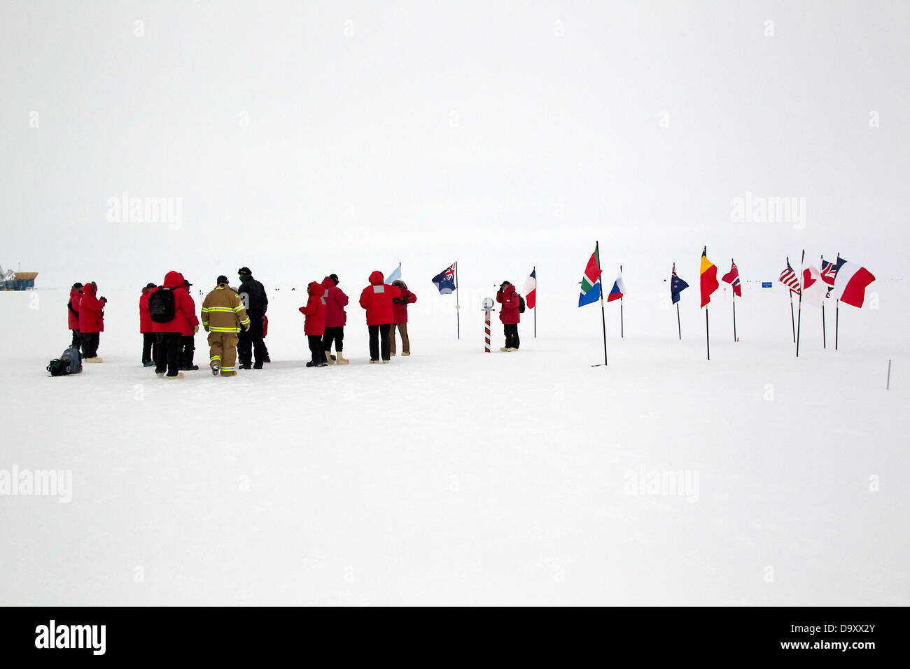 I visitatori per il cerimoniale di polo sud marker con le bandiere del trattato antartico unite, Polo Sud Antartide Foto Stock