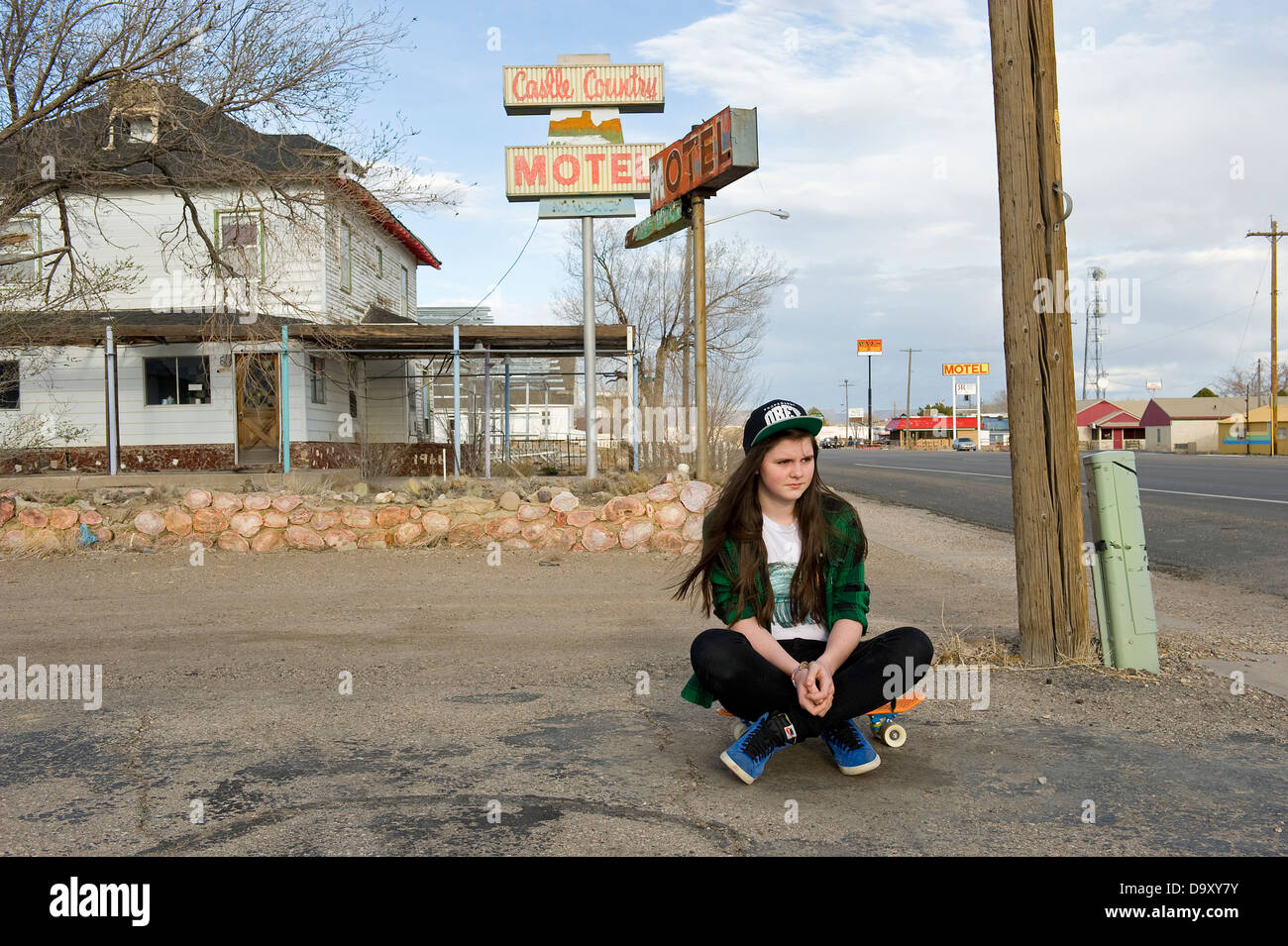 Ragazza adolescente con lo skateboard seduto fuori casa indossando obbedire a cappuccio verde e verificata la maglietta, Green River, Utah, Stati Uniti d'America. Foto Stock