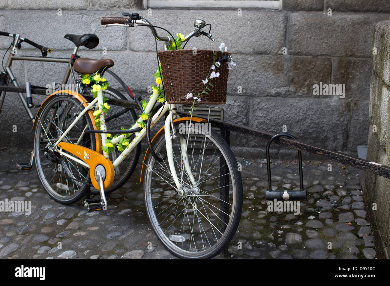 Bicicletta a passo decorata con fiori con un cestino anteriore parcheggiata accanto a un muro di pietra a Dublino, Irlanda, nel 2013. Foto Stock