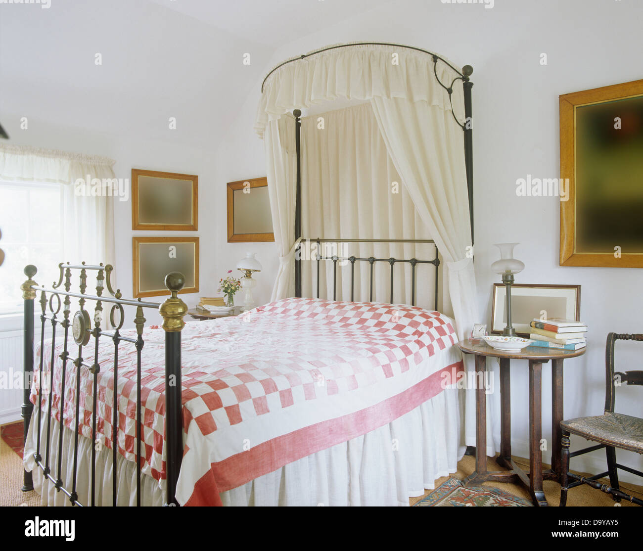 Tettoia in metallo con il bianco voile drappeggi su in ottone antico letto con rosa+trapunta bianca nel paese camera da letto con comodino Foto Stock